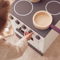 Child turning the knobs of the white wooden toy stove with wooden pots on the hob